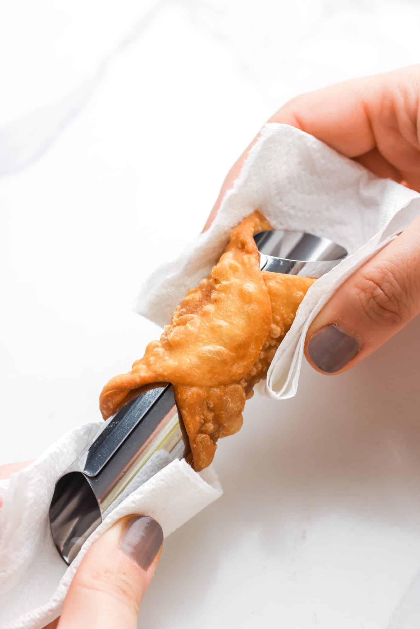 a person carefully removing a cannoli shell from a metal form using paper towels. 