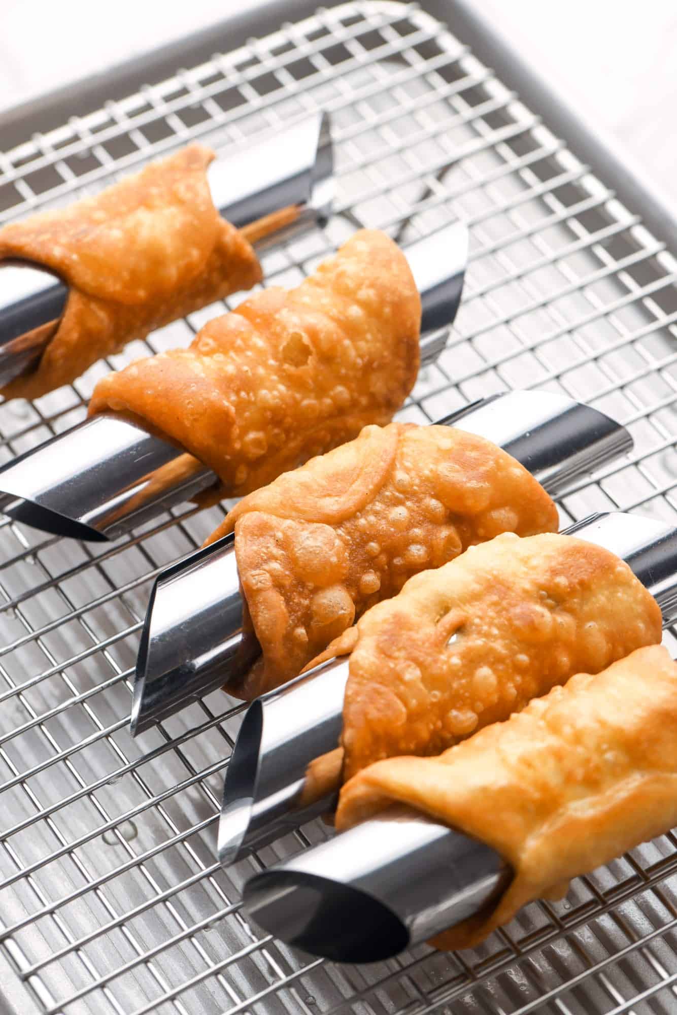 fried cannoli shells cooling on a wire rack while still on their forms. 