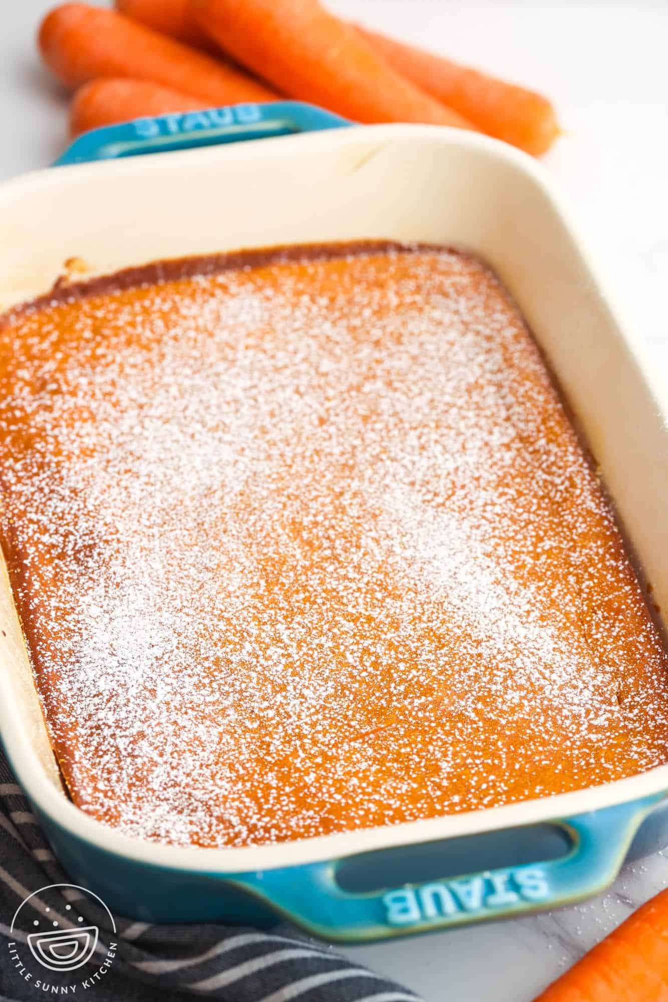 Carrot Souffle baked in a Staub dish, sprinkled with powdered sugar. And fresh carrots are in the background.