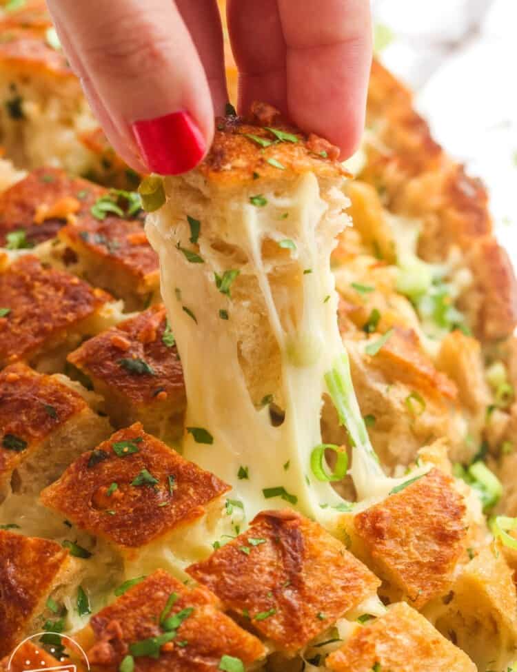 cheesy garlic pull apart bread. A hand is picking up a piece, showing the cheese pull.