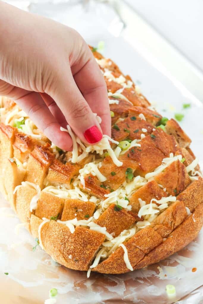 a hand stuffing a loaf of bread with cheese.