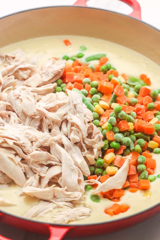 shredded chicken and frozen veggies added to a pan of sauce.