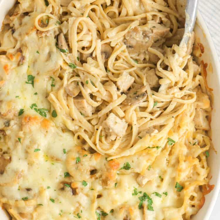 chicken tetrazzini in a casserole dish, served with a pair of tongs.