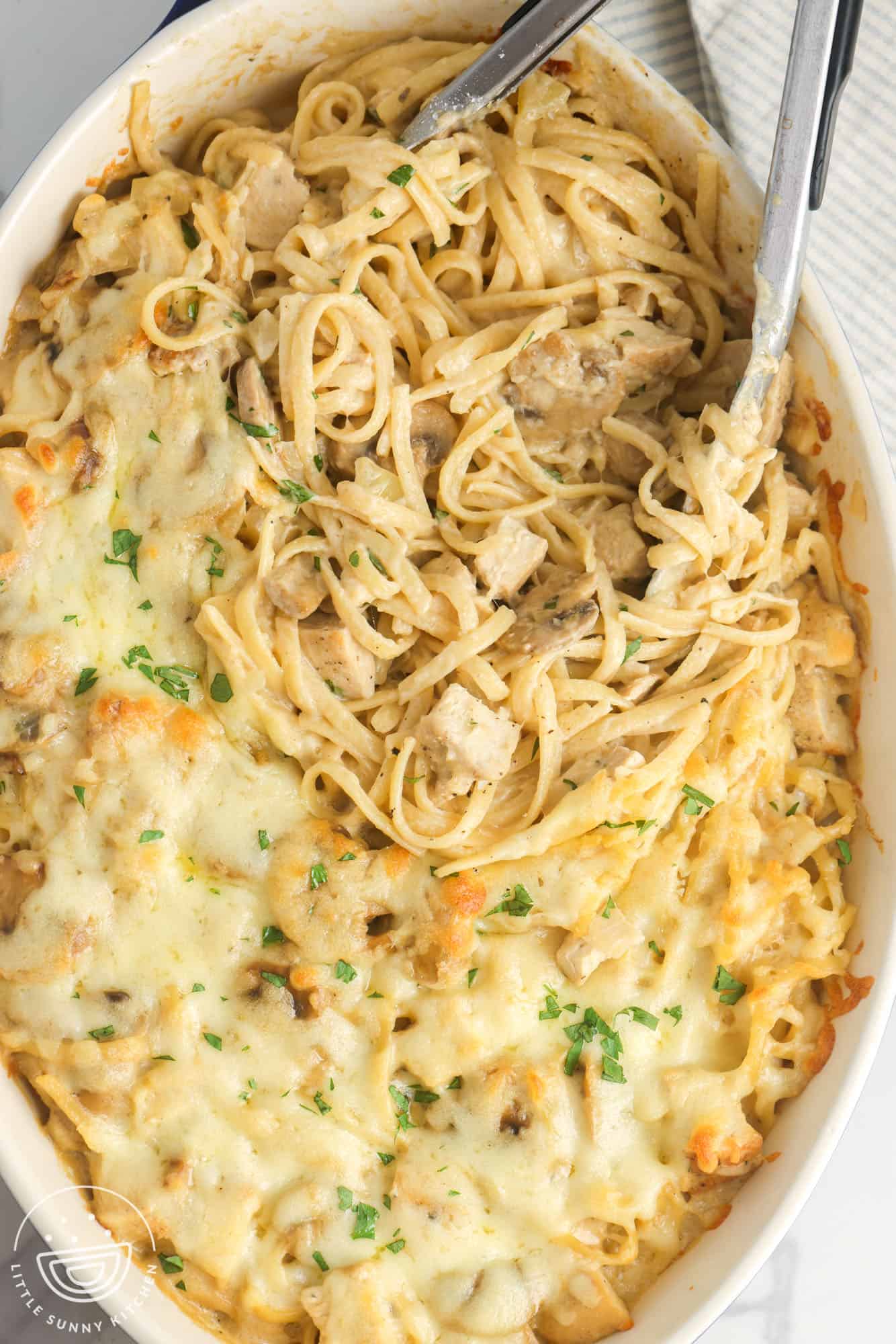 chicken tetrazzini in a casserole dish, served with a pair of tongs.