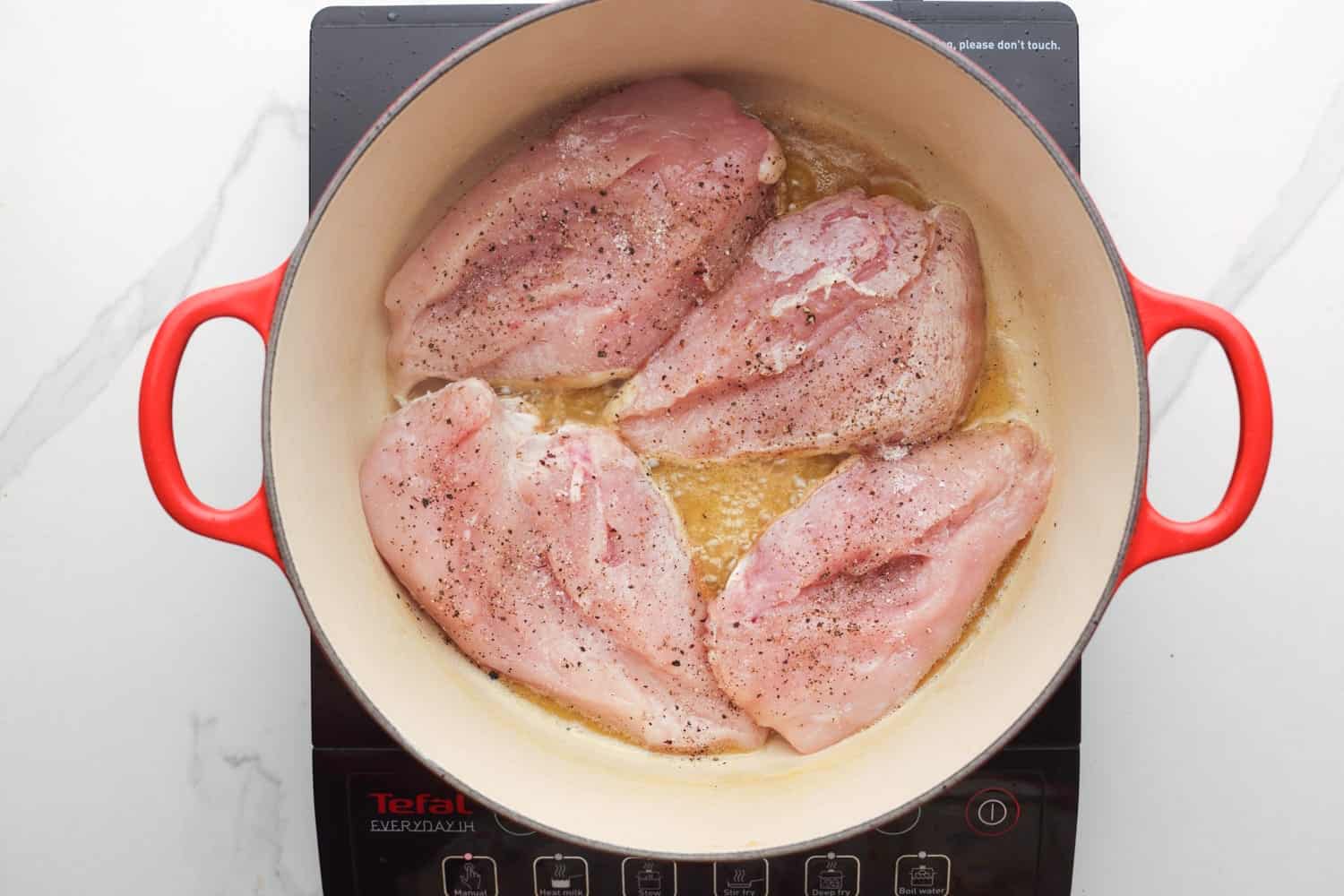 4 raw chicken breasts in a pot with oil and butter.