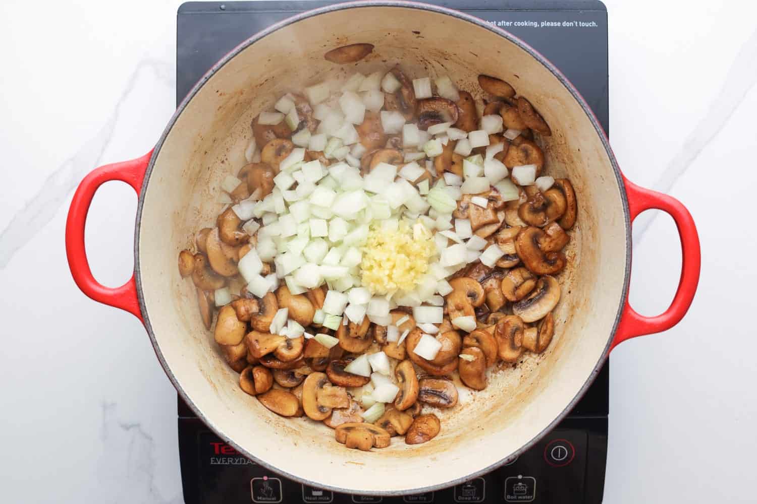 diced onion and minced garlic added to cooked button mushrooms in a pot.