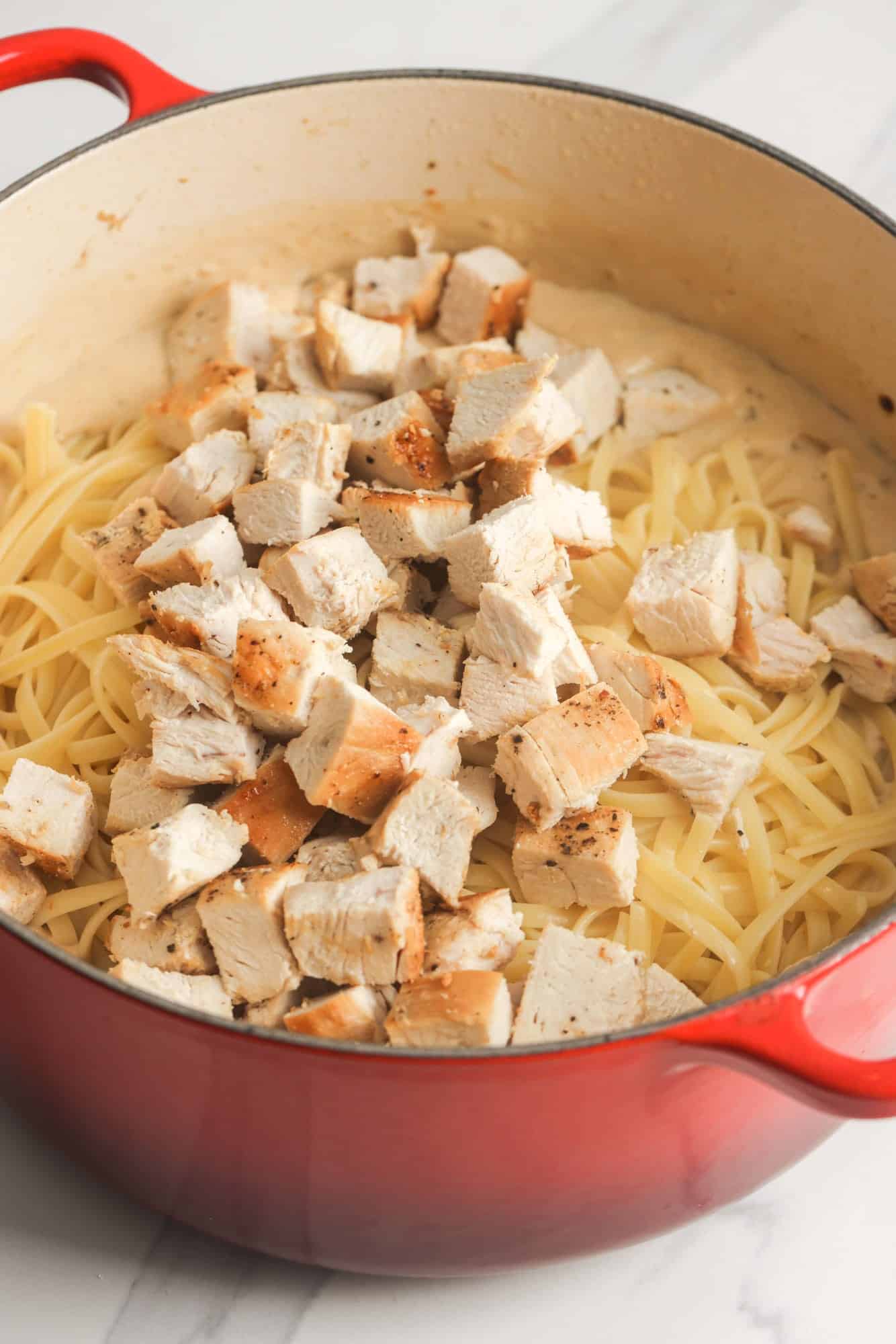 diced chicken added to pasta and tetrazzini sauce in a pan