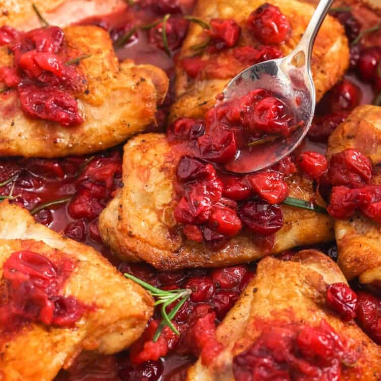 a spoon adding cooked cranberries to the top of cooked chicken thighs in a skillet.