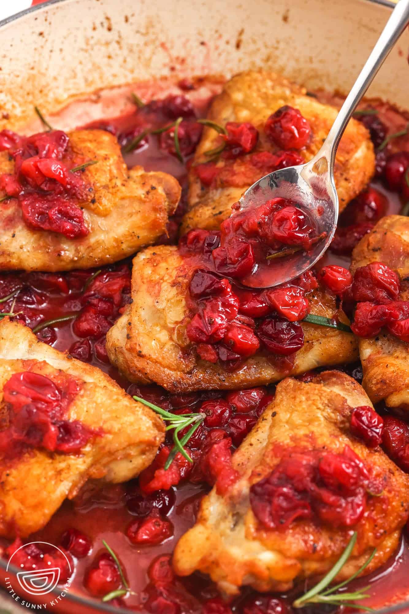 a spoon adding cooked cranberries to the top of cooked chicken thighs in a skillet.