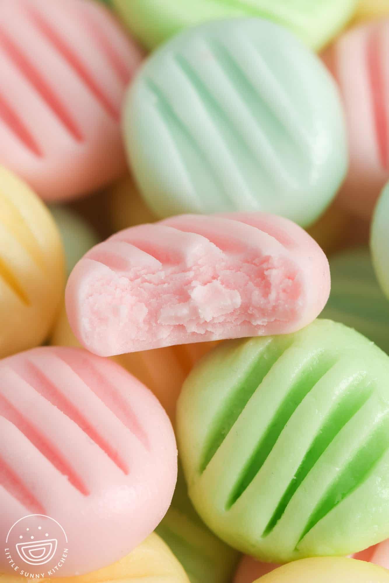 closeup of pastel cream cheese mints. One has a bite taken to show the fluffy inside.