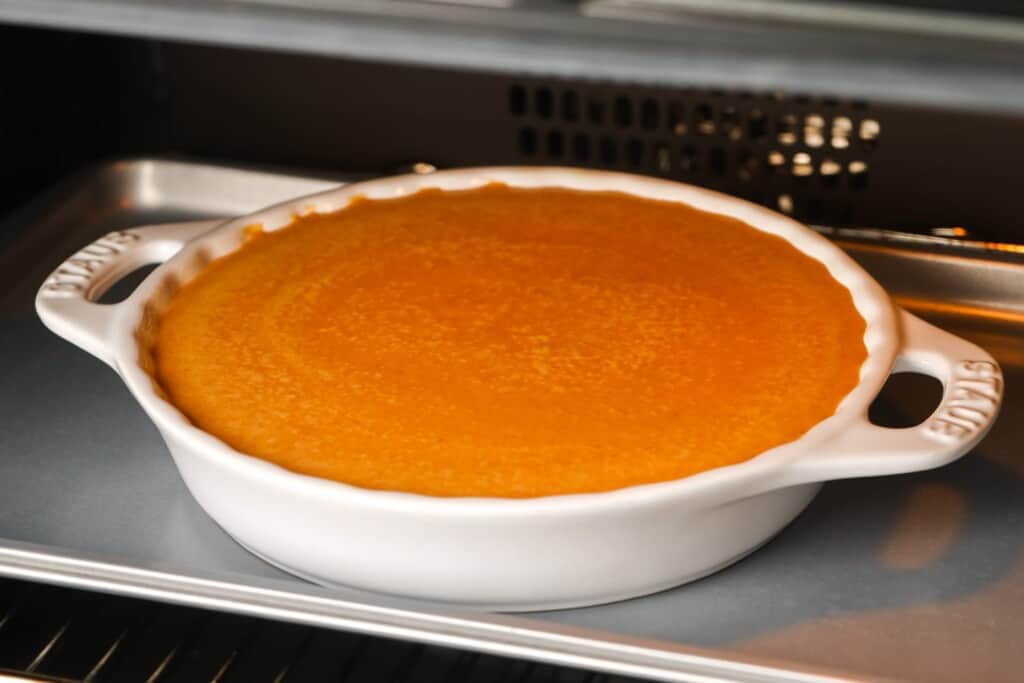 a white ceramic pie plate on a sheet pan holding pumpkin pie filling.