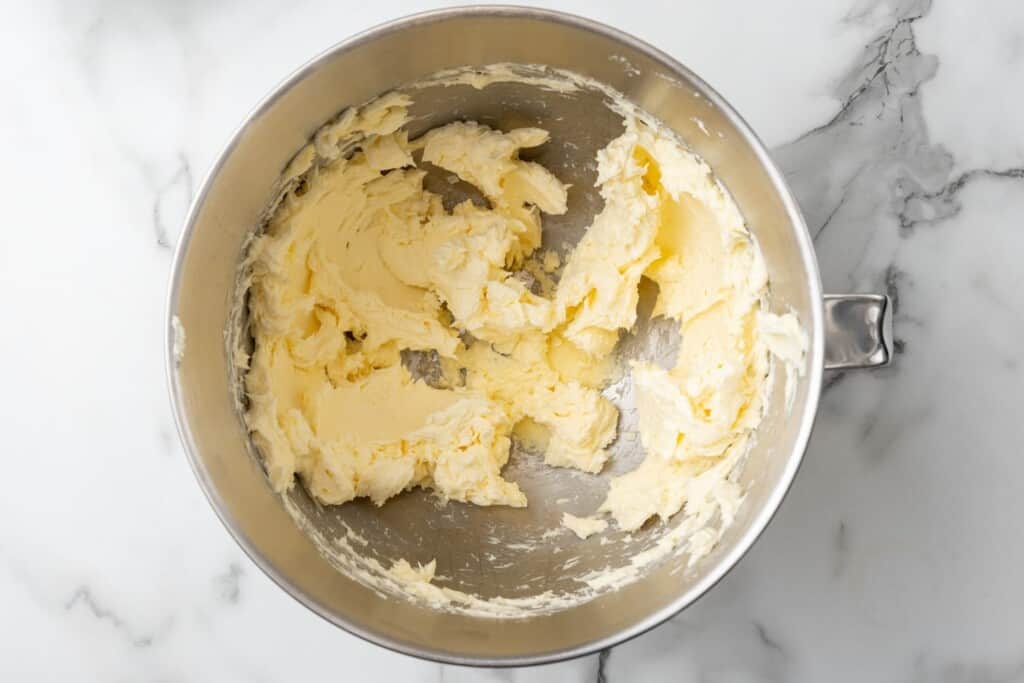 creamed butter and cream cheese in the bowl of a stand mixer, viewed from overhead. The bowl is on a marble counter.