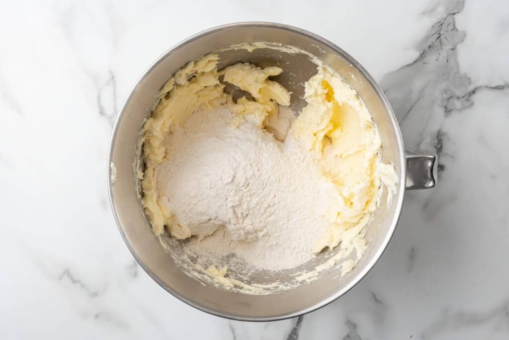 flour added to creamed butter in a silver kitchenaid mixer bowl.