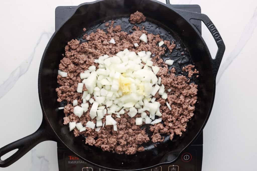 diced onions added to browned ground beef in a skillet.