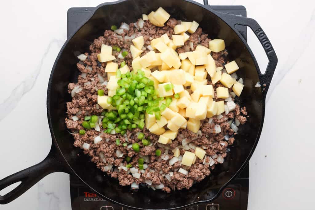 ground beef in a skillet with onion, green pepper, and diced potatoes.