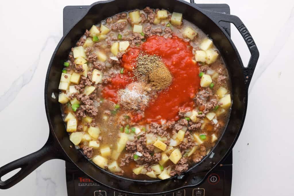 mexican picadillo cooking in a skillet with herbs and tomatoes.