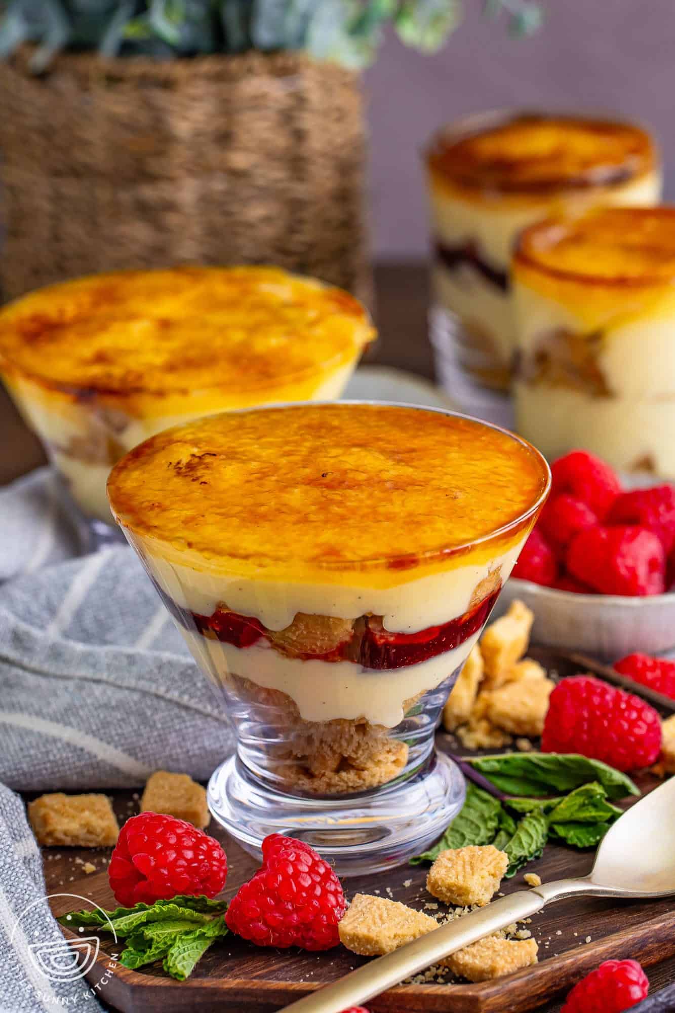 Mini creme brulee trifles in dessert cups, with fresh raspberries on the sides.