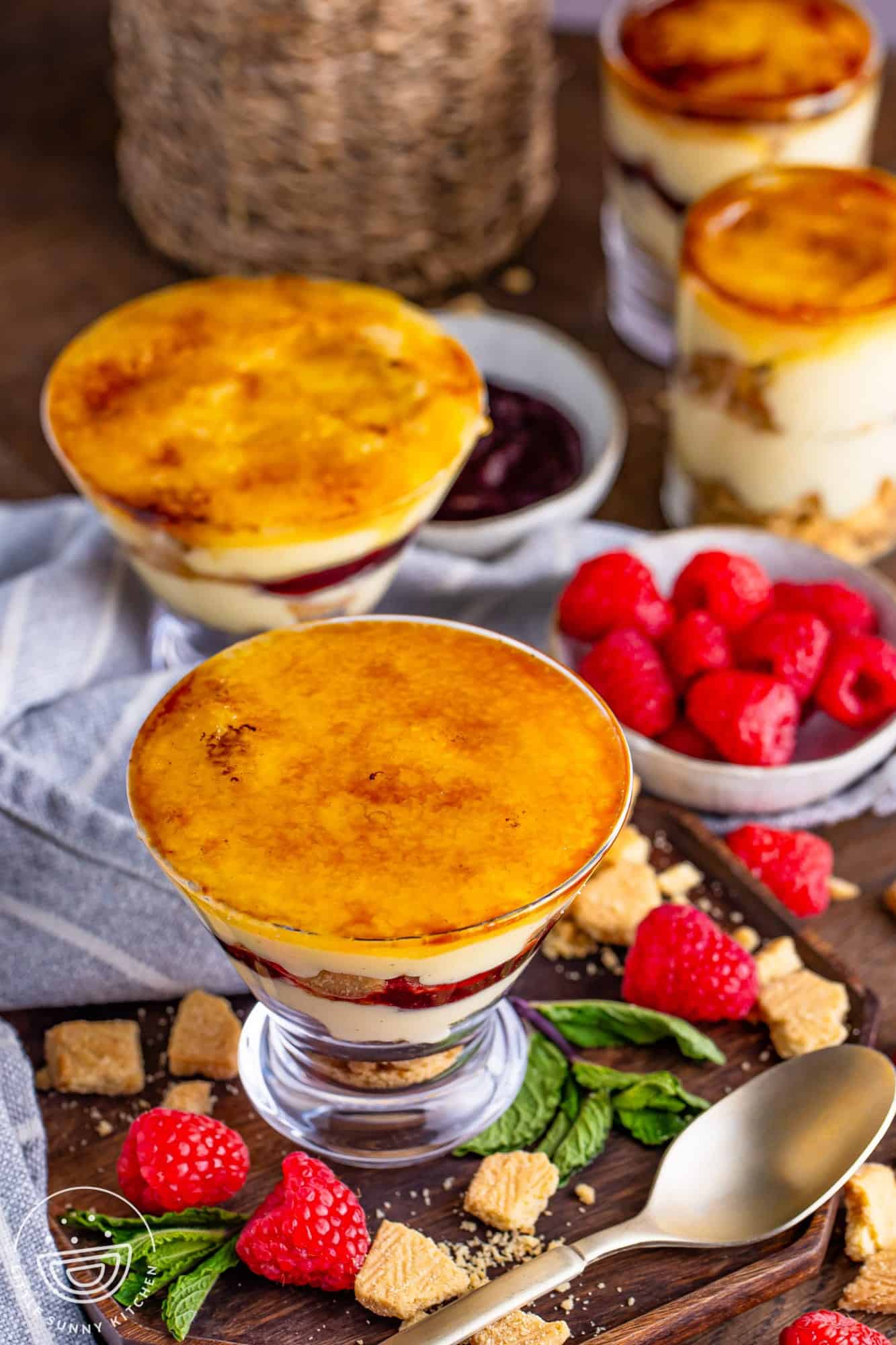 4 cups of creme brulee trifles, with fresh raspberries on the sides.