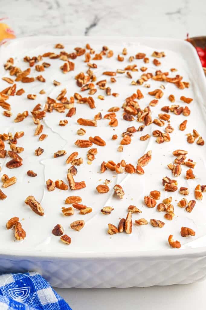 Angle shot of a no bake twinkie cake topped with white whipped topping and pecan pieces, in a 9x13 white ceramic dish.