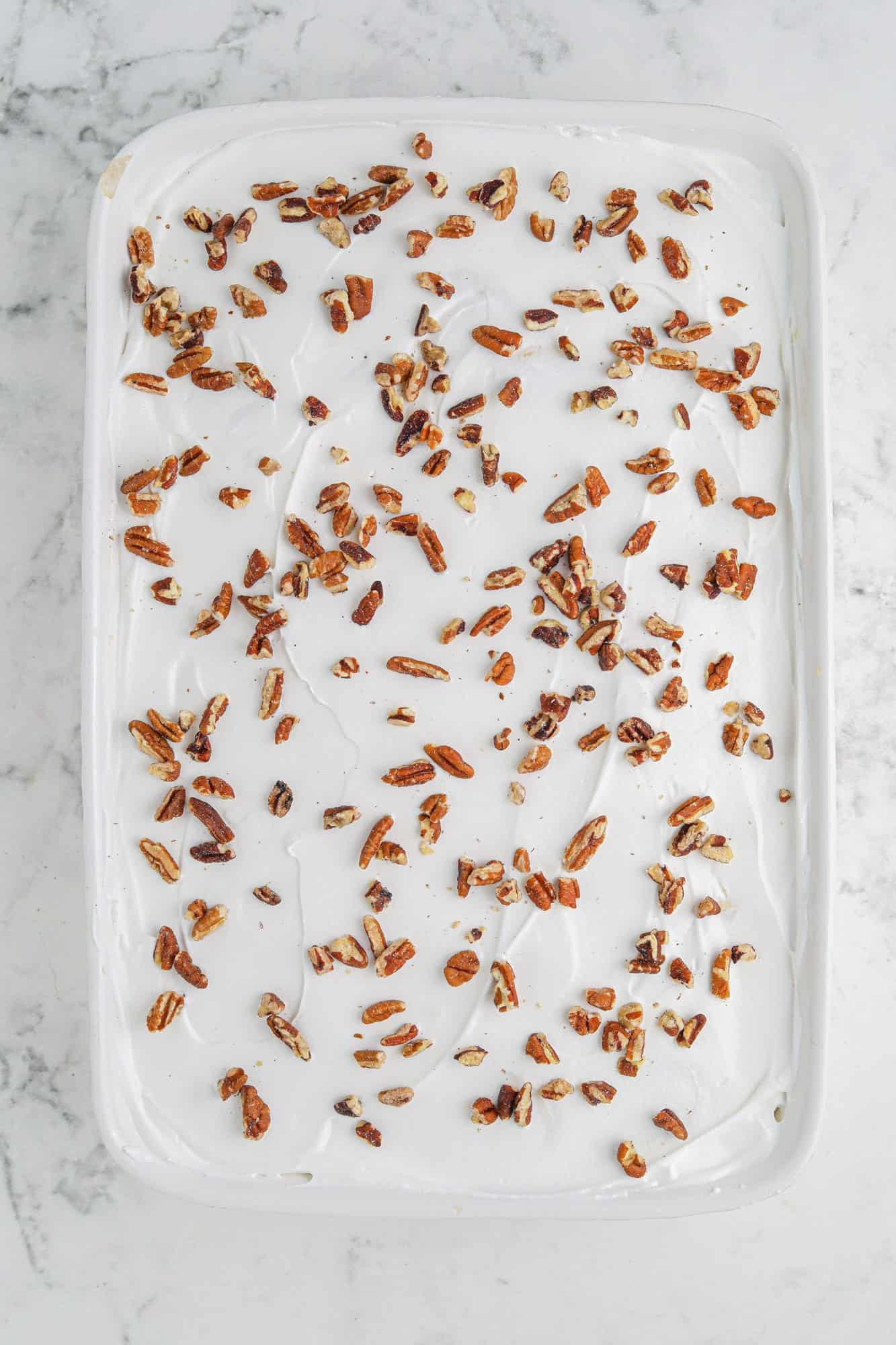 whipped topping topped with pecan pieces in a 9x13 ceramic white dish