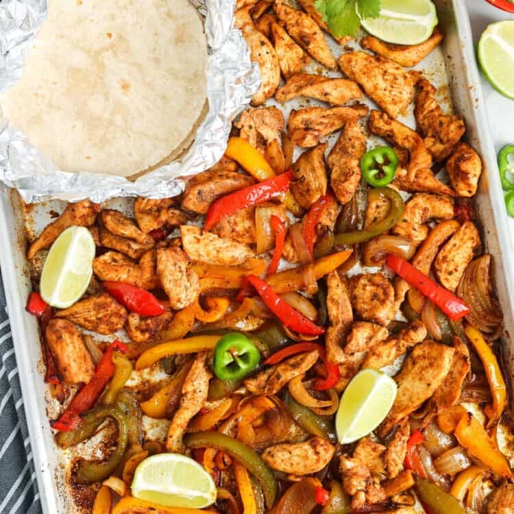 a sheet pan filled with chicken fajitas and warmed tortillas in foil.