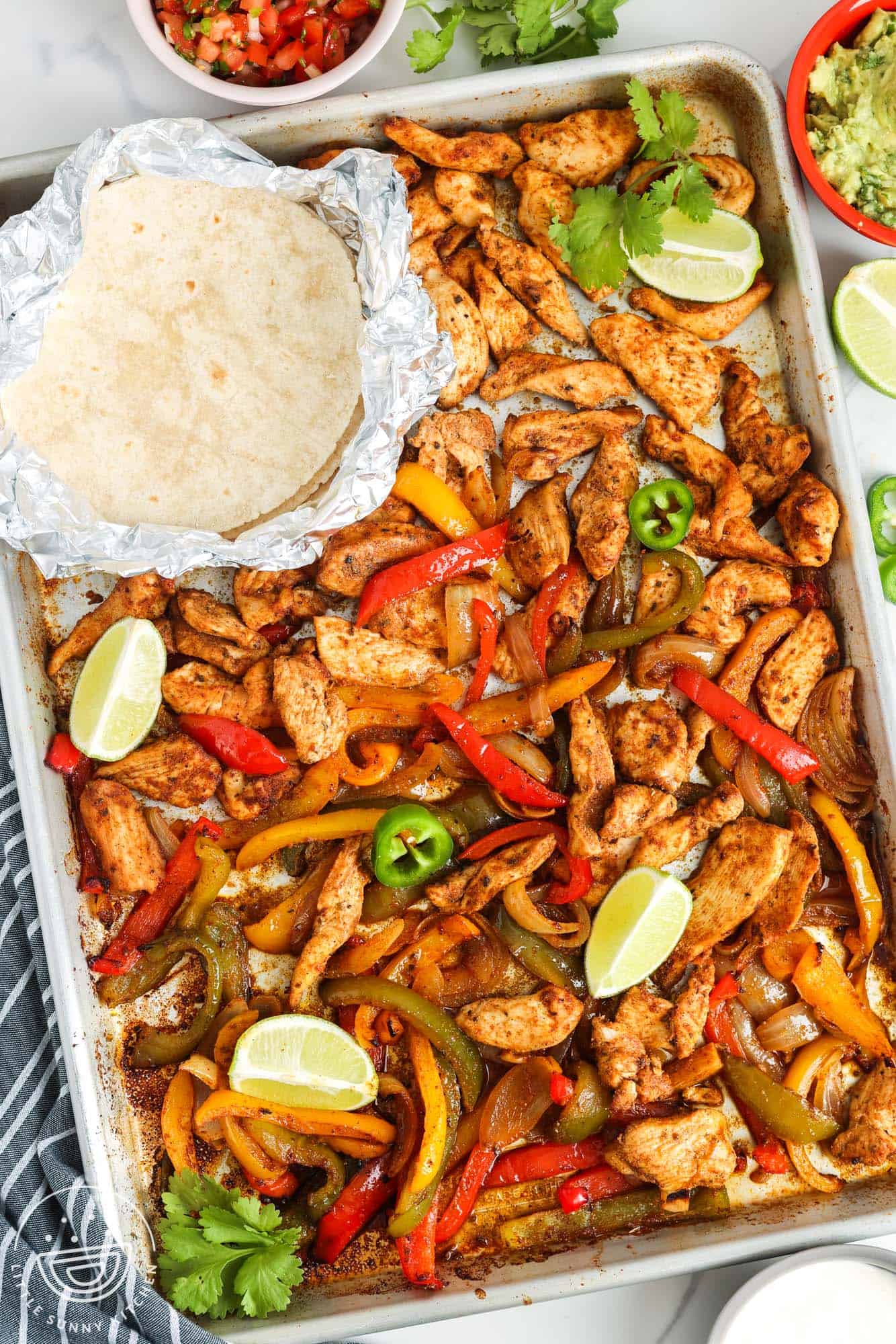 a sheet pan filled with chicken fajitas and warmed tortillas in foil.