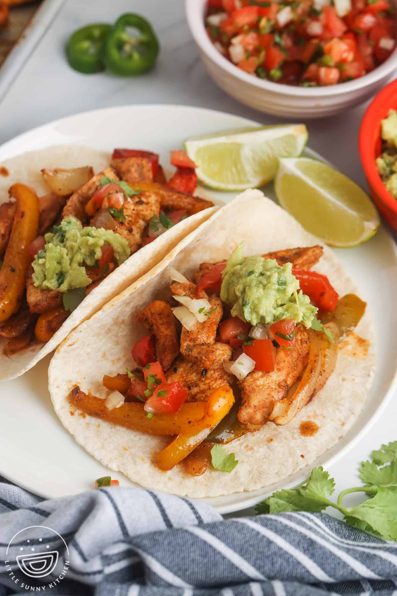 two chicken fajitas on flour tortillas on a plate, topped with pico and guac