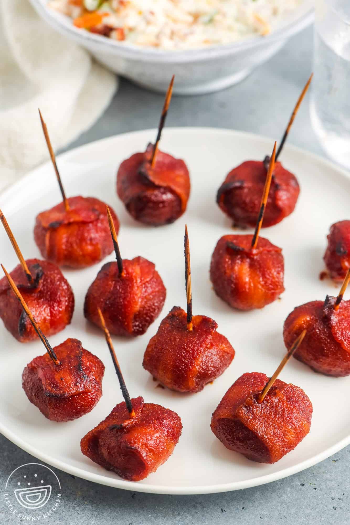 a white plate holding baked chestnuts marinated in red sauce and wrapped with bacon.