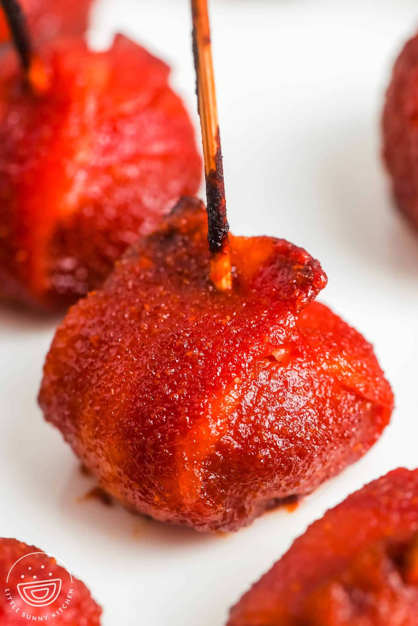 closeup of a bacon wrapped water chestnut coated in a sweet ketchup glaze, speared onto a toothpick.