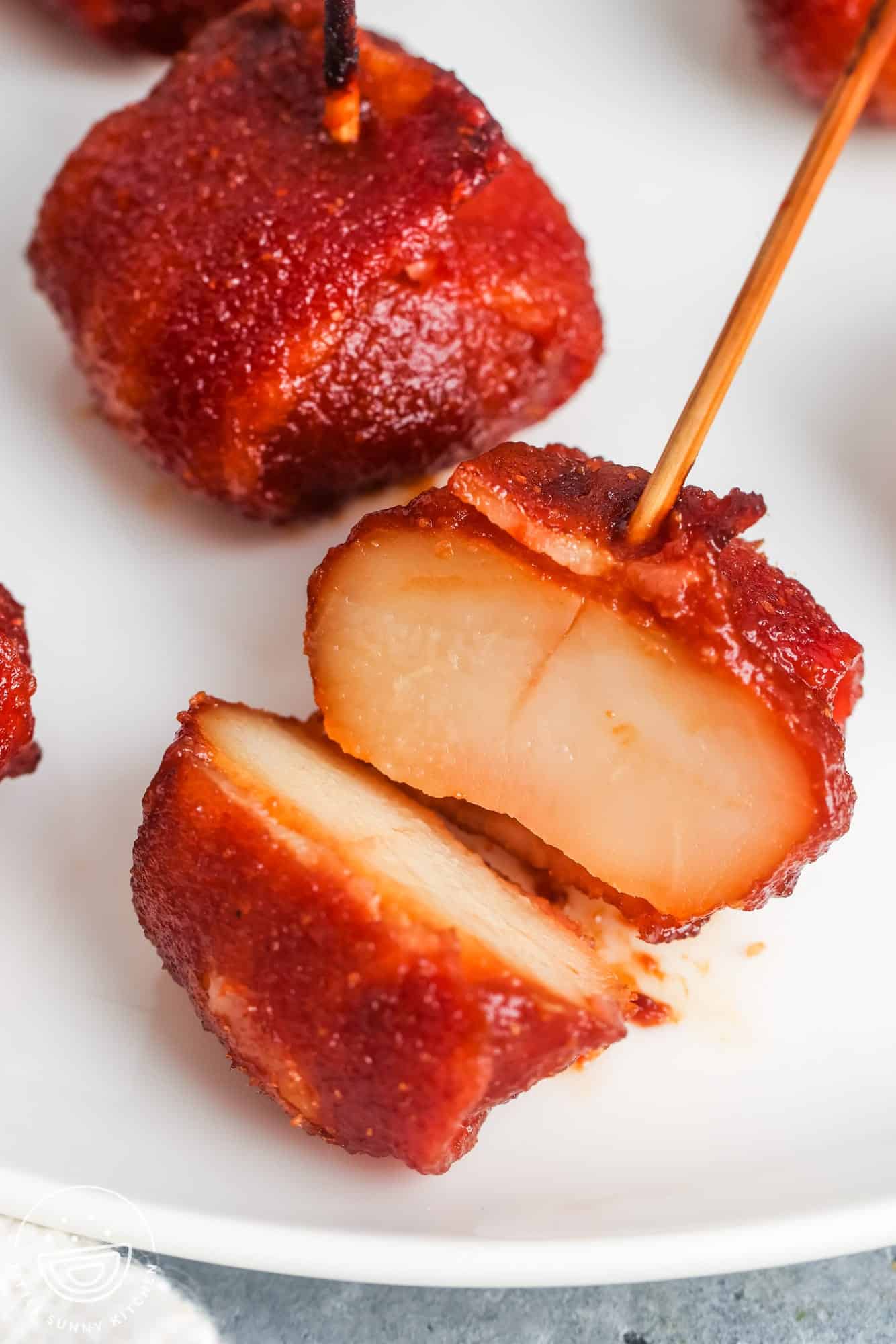 closeup view of a bacon wrapped water chestnut on a toothpick, it's cut in half to show what the inside looks like. 