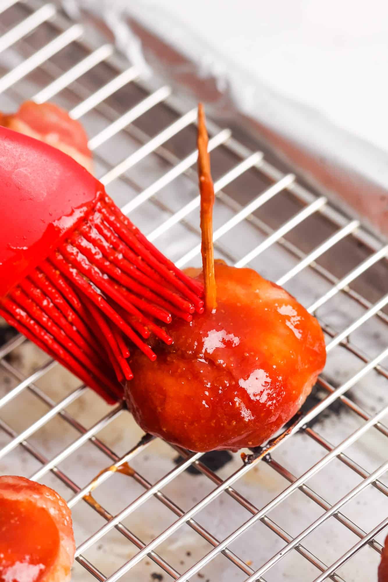 a red silicone basting brush adding extra glaze to a baked bacon wrapped water chestnut. 