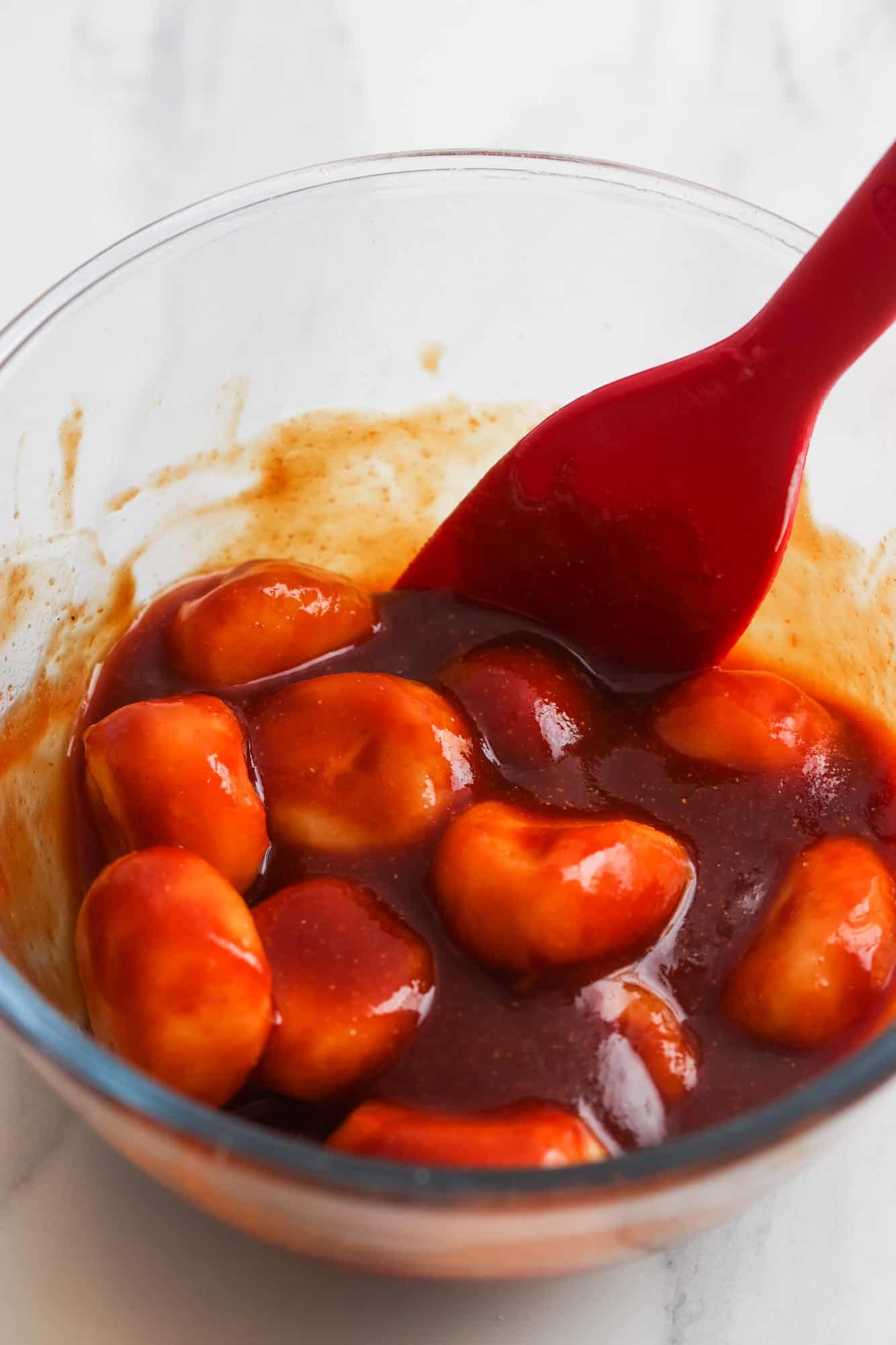 water chestnuts marinating in a red glaze. A red spoon is stirring them in a glass bowl. 