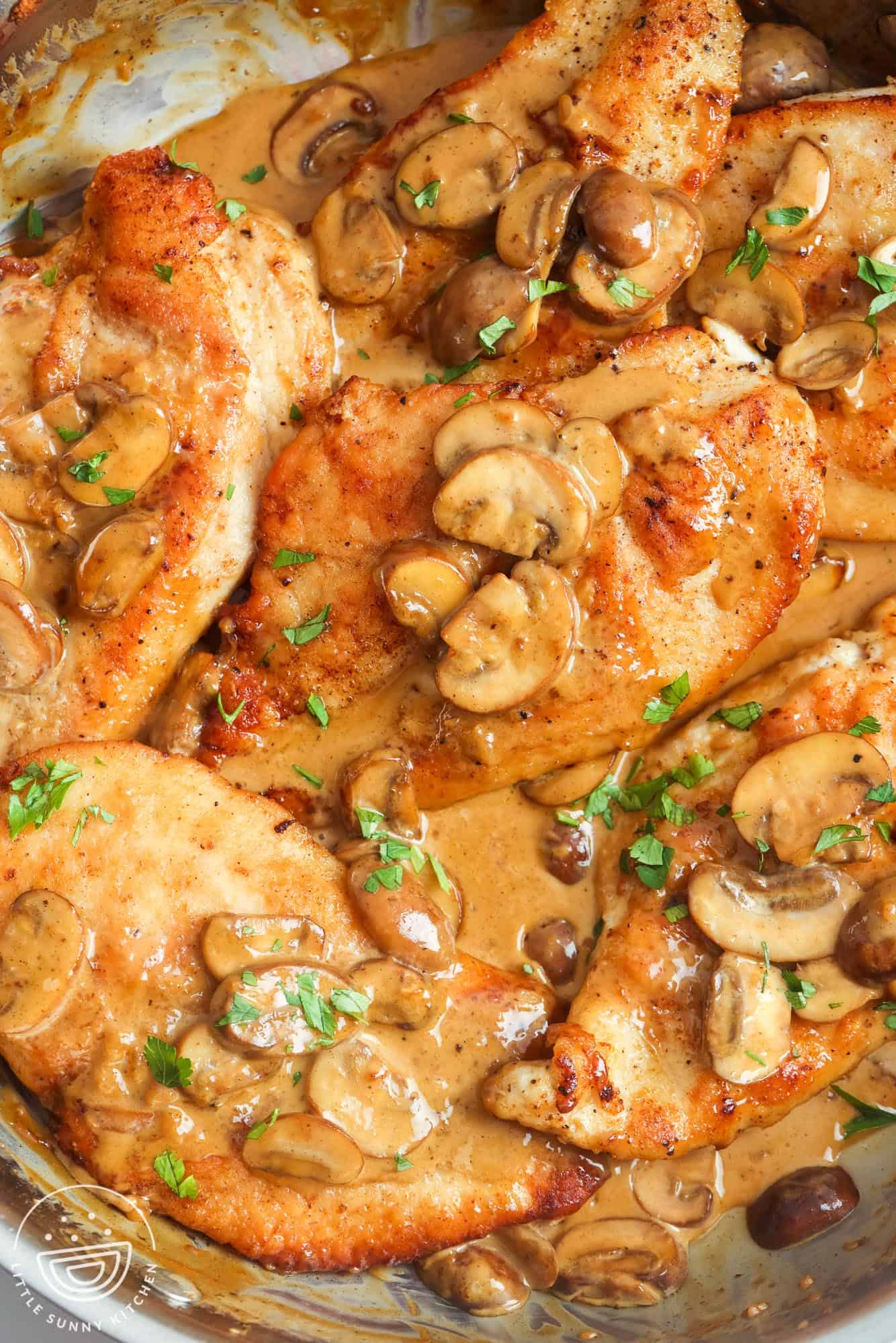 chicken cutlets in marsala wine sauce with mushrooms, in a stainless steel skillet. 