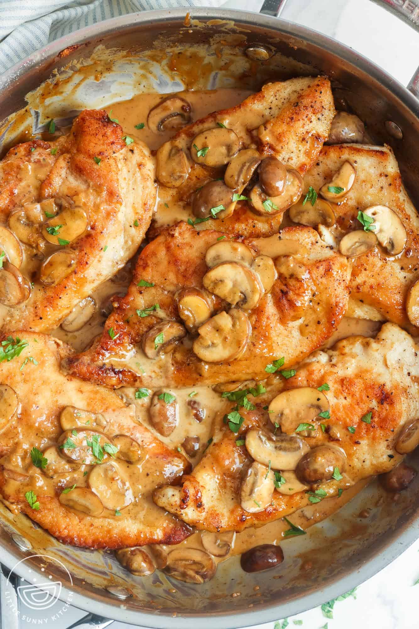 Browned chicken cutlets with mushrooms in a marsala sauce, all in a stainless steel skillet. 