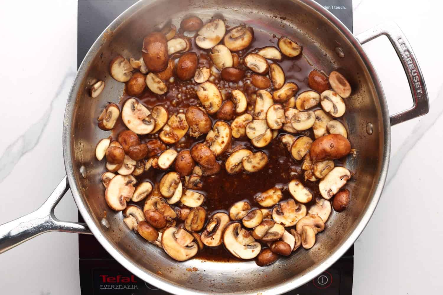 a skillet of sliced mushrooms being cooked with marsala wine