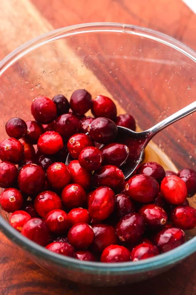 a bowl of fresh cranberries, tossed with brown sugar and orange juice.