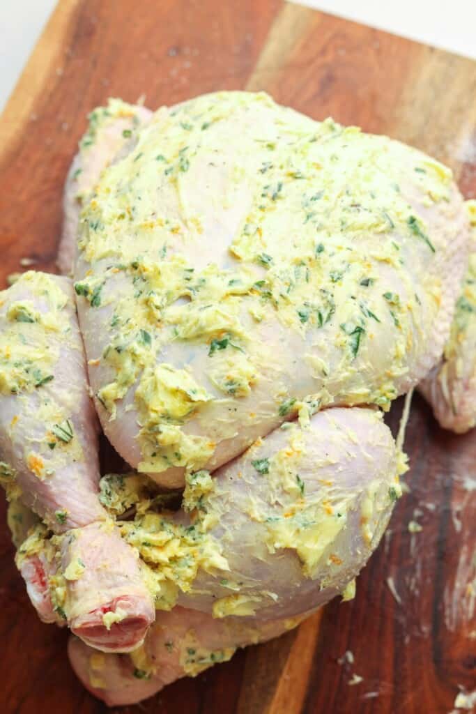 a raw chicken that has been tied together and coated in herb butter.