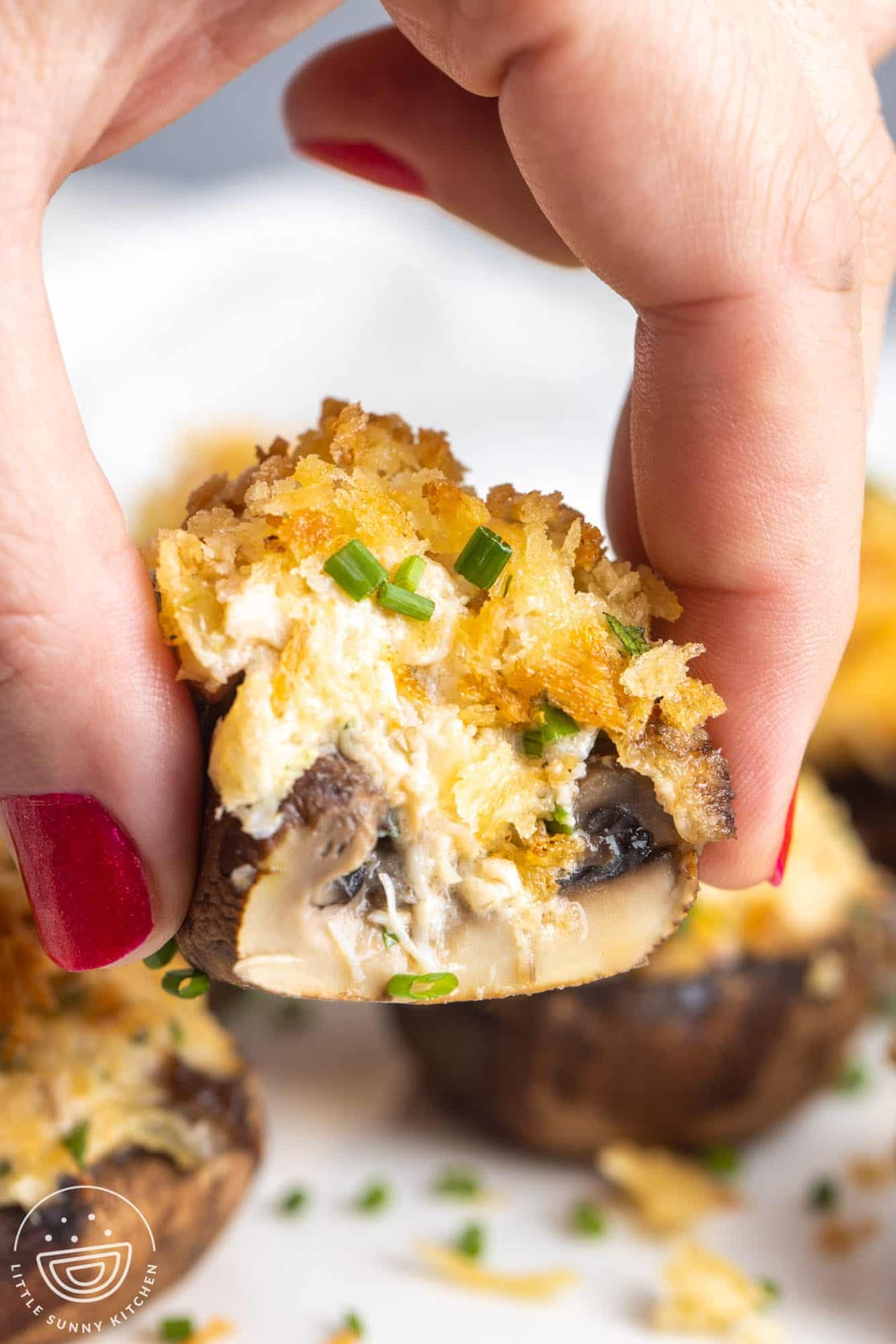 a hand holding half of a crab stuffed mushroom garnished with chive