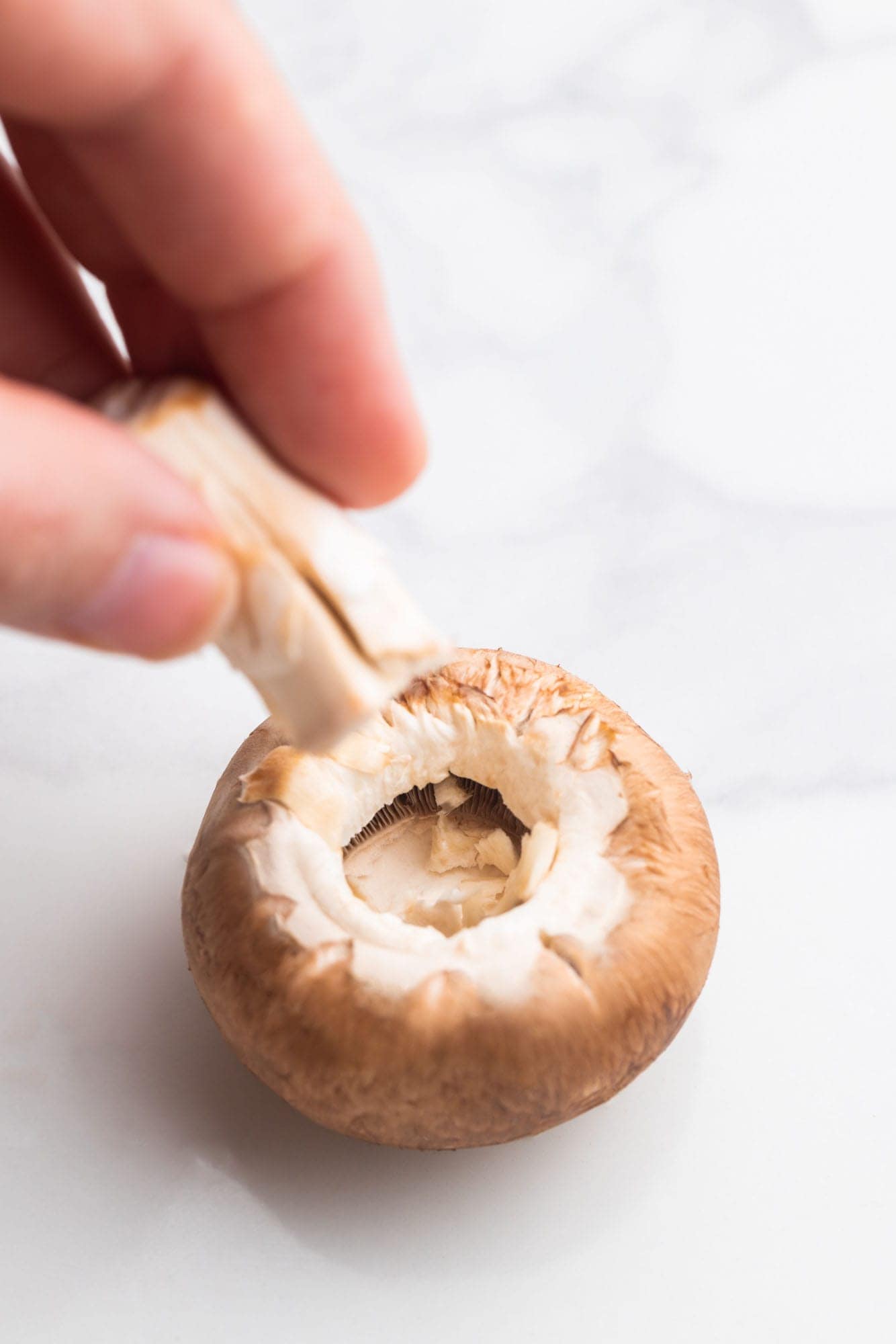 a hand pulling the stem from a cremini mushroom.