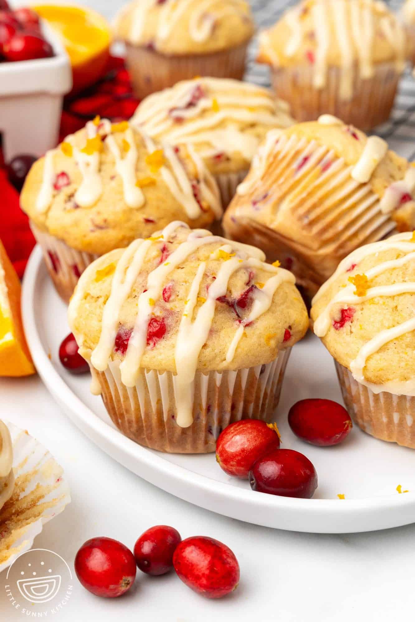 a white plate holding several homemade cranberry orange muffins with orange glaze.