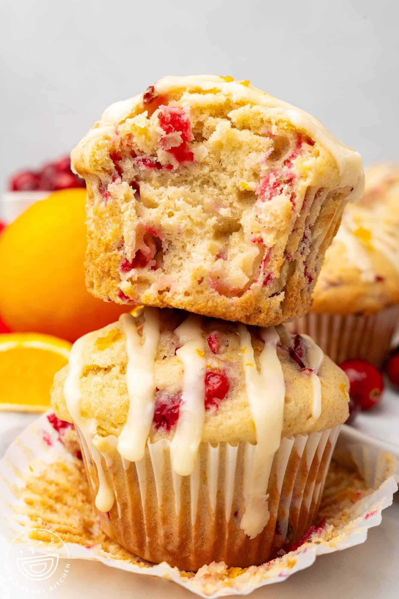 two homemade cranberry orange muffins stacked. The top one has had a bite taken to show the tender interior