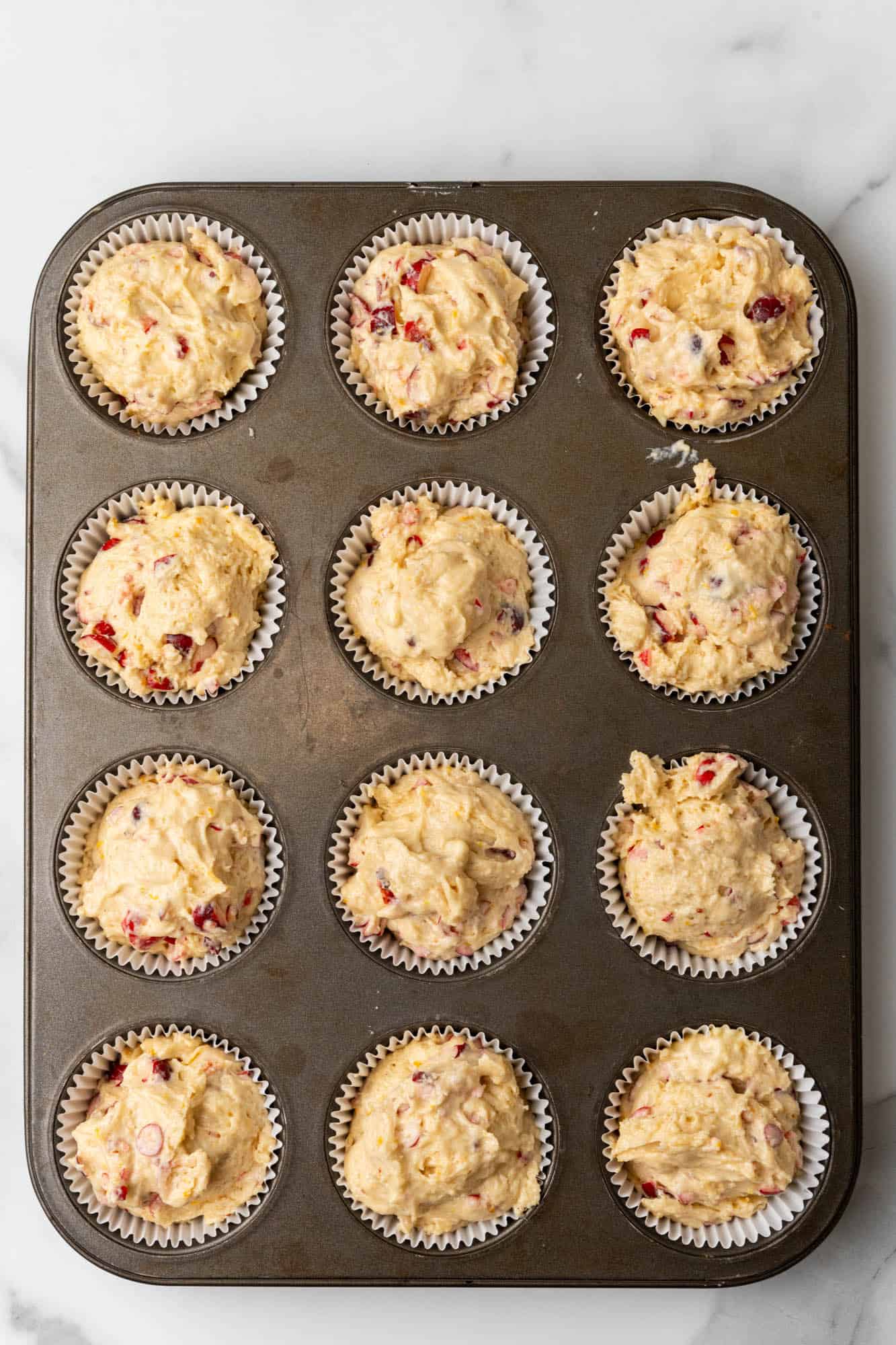 Muffin cups filled with cranberry batter, to the top. 