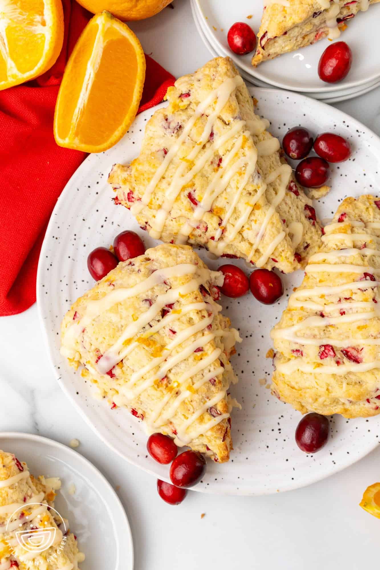 top down view of three orange cranberry scones on a ceramic plate with an orange glaze drizzle. 