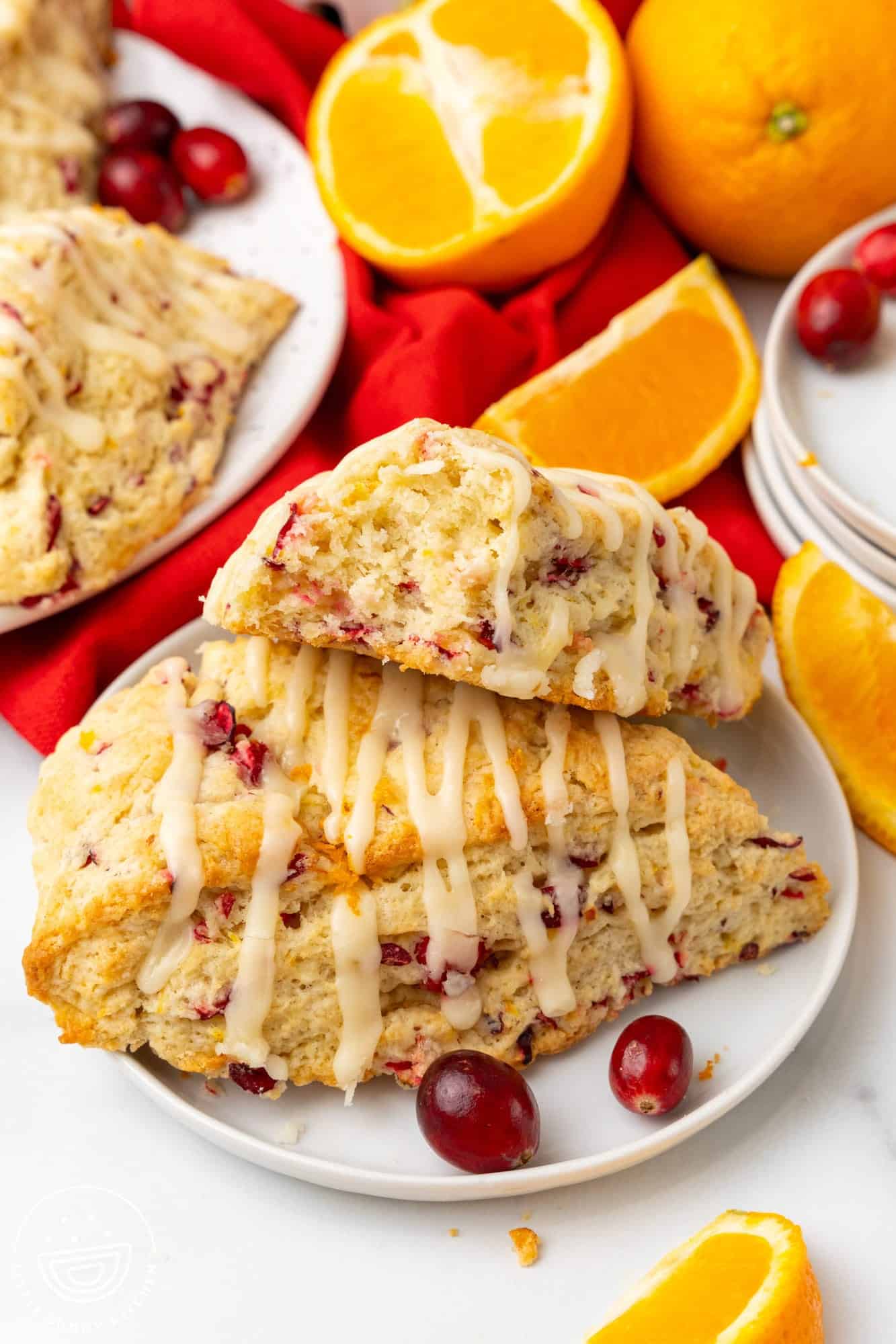 a small white plate holding two cranberry orange scones with glaze. One has a bite taken to show the tender and moist interior. 