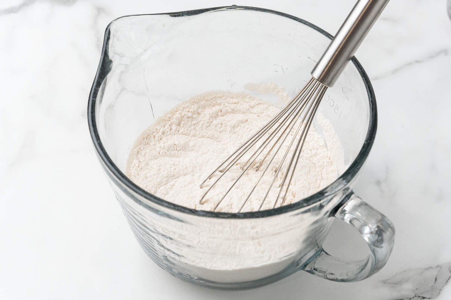 Flour in a large glass mixing bowl with a whisk. 