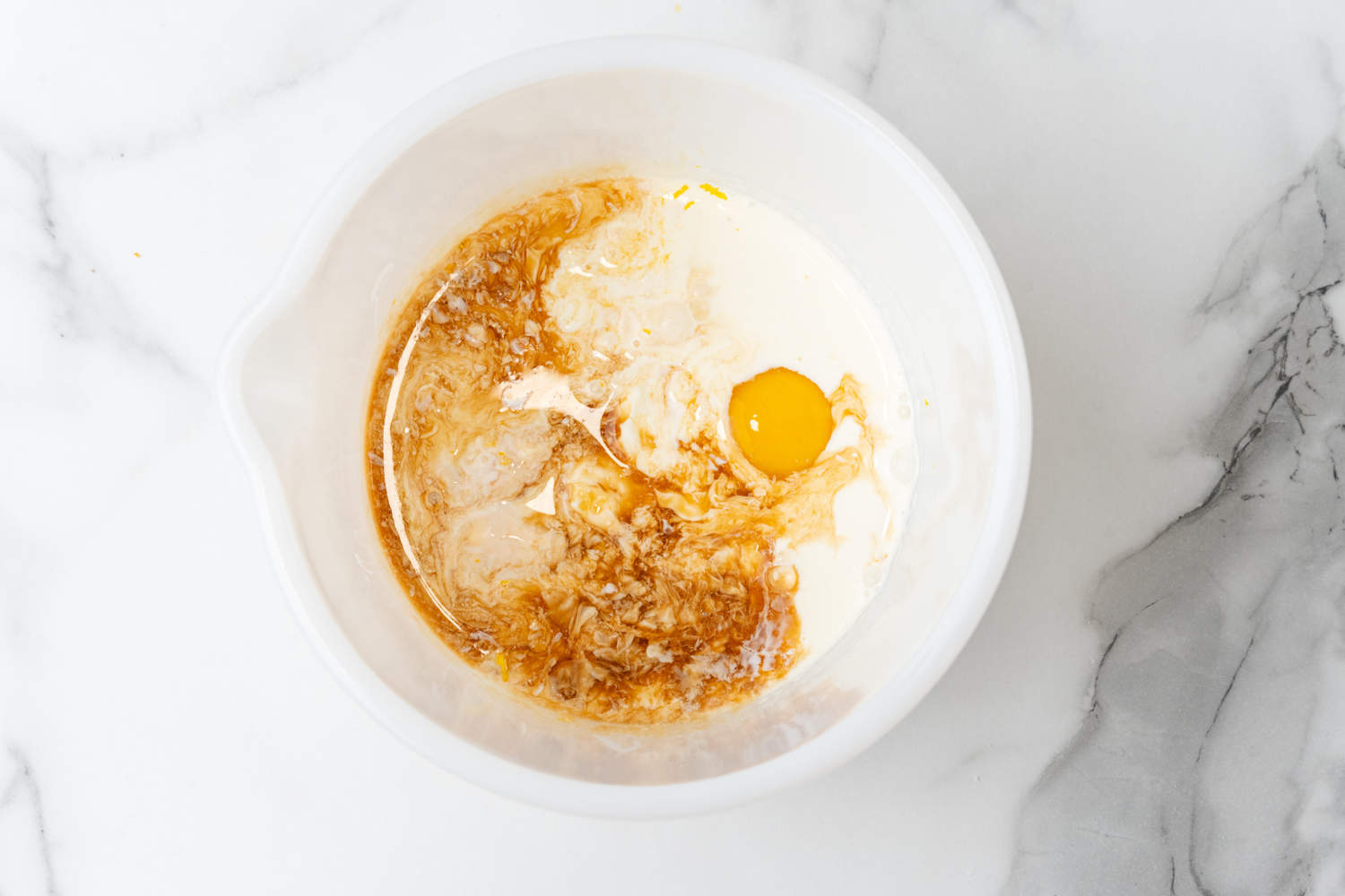 cream and sugar with vanilla extract and an egg in a white mixing bowl. 