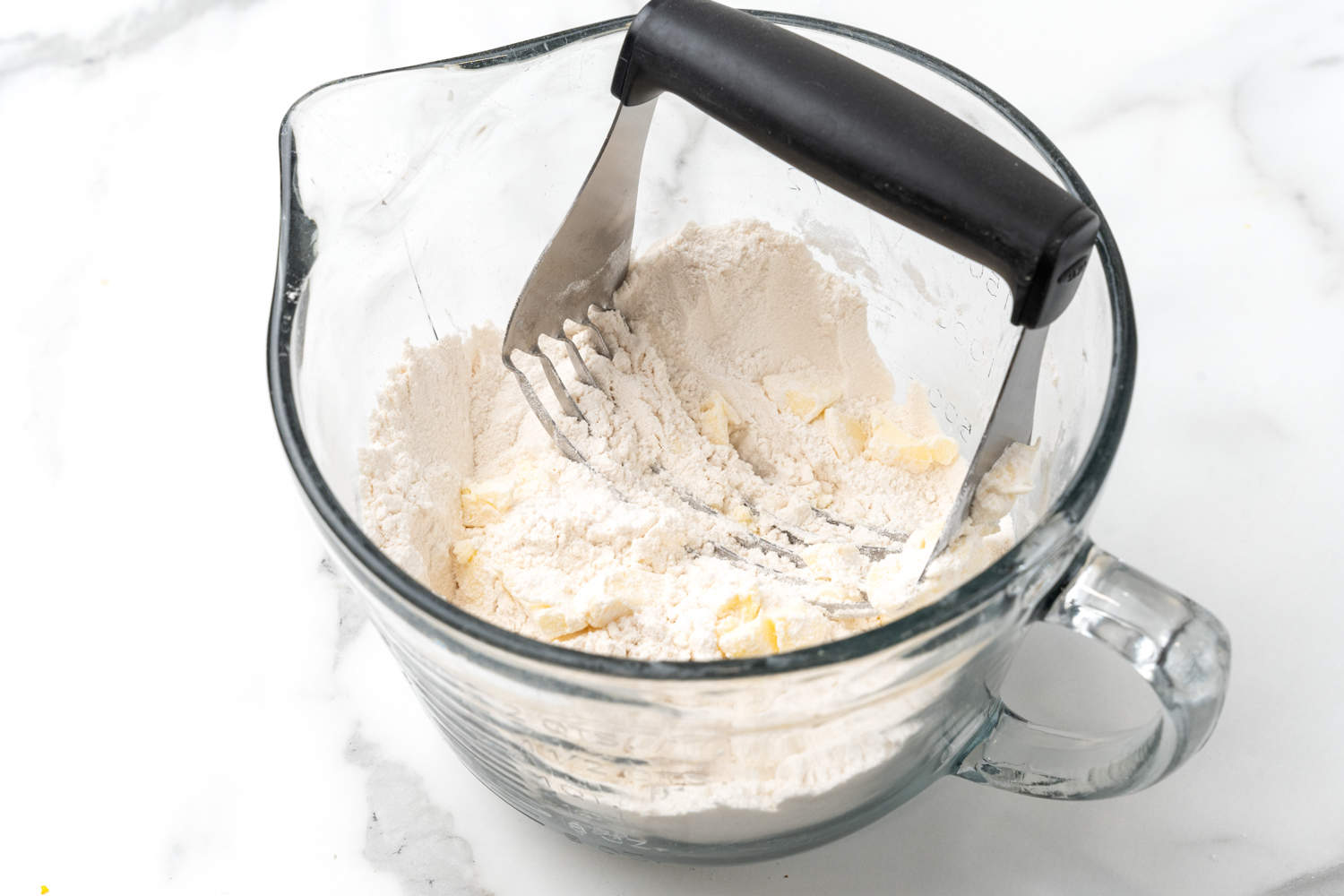 a pastry cutter blending flour and cold butter together in a large glass measuring cup. 