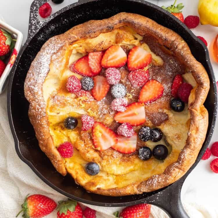 overhead shot of a baked dutch baby pancake topped with fresh berries and powdered sugar.