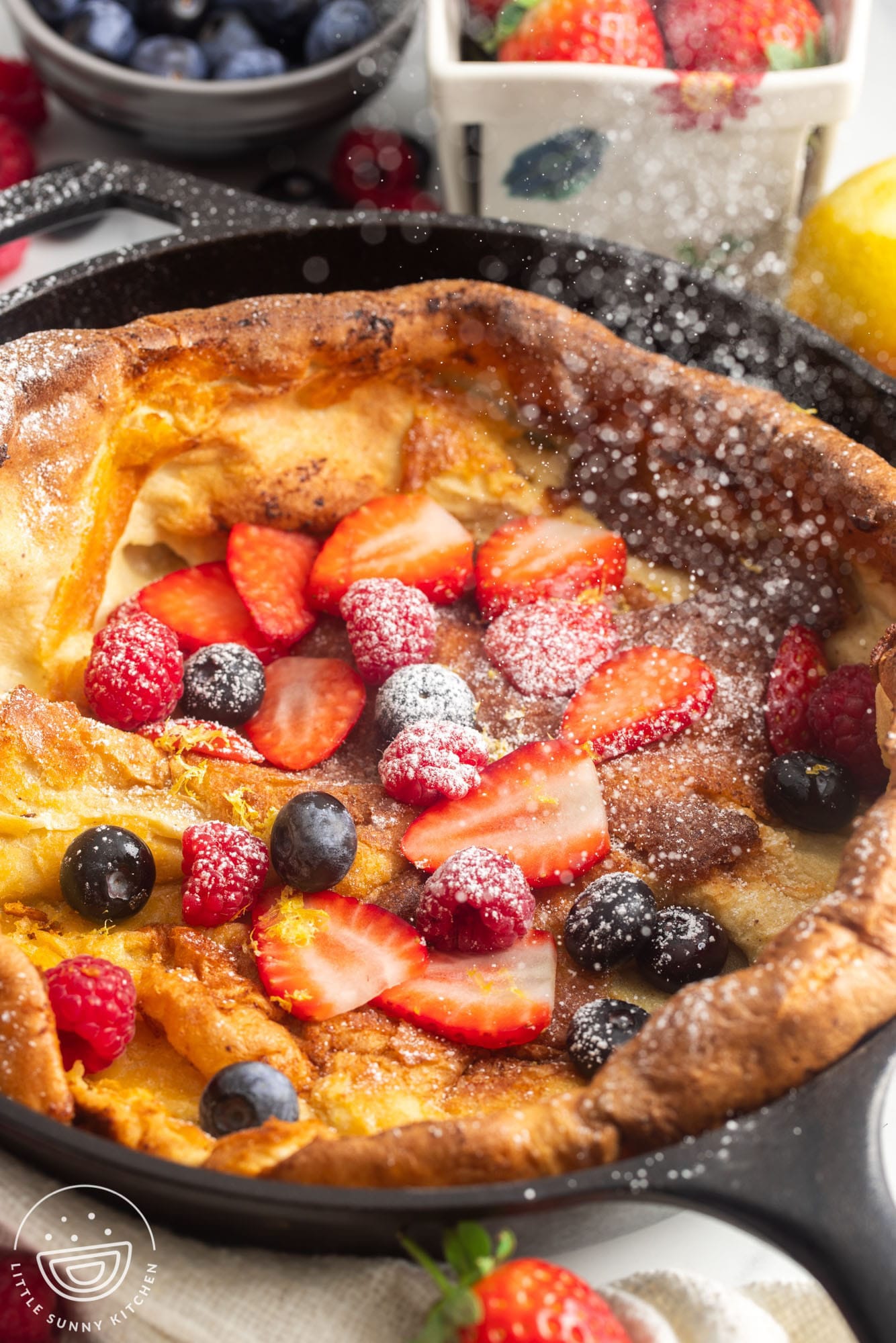 powdered sugar dusted over a freshly cooked dutch baby pancake, topped with fresh berries and lemon zest.