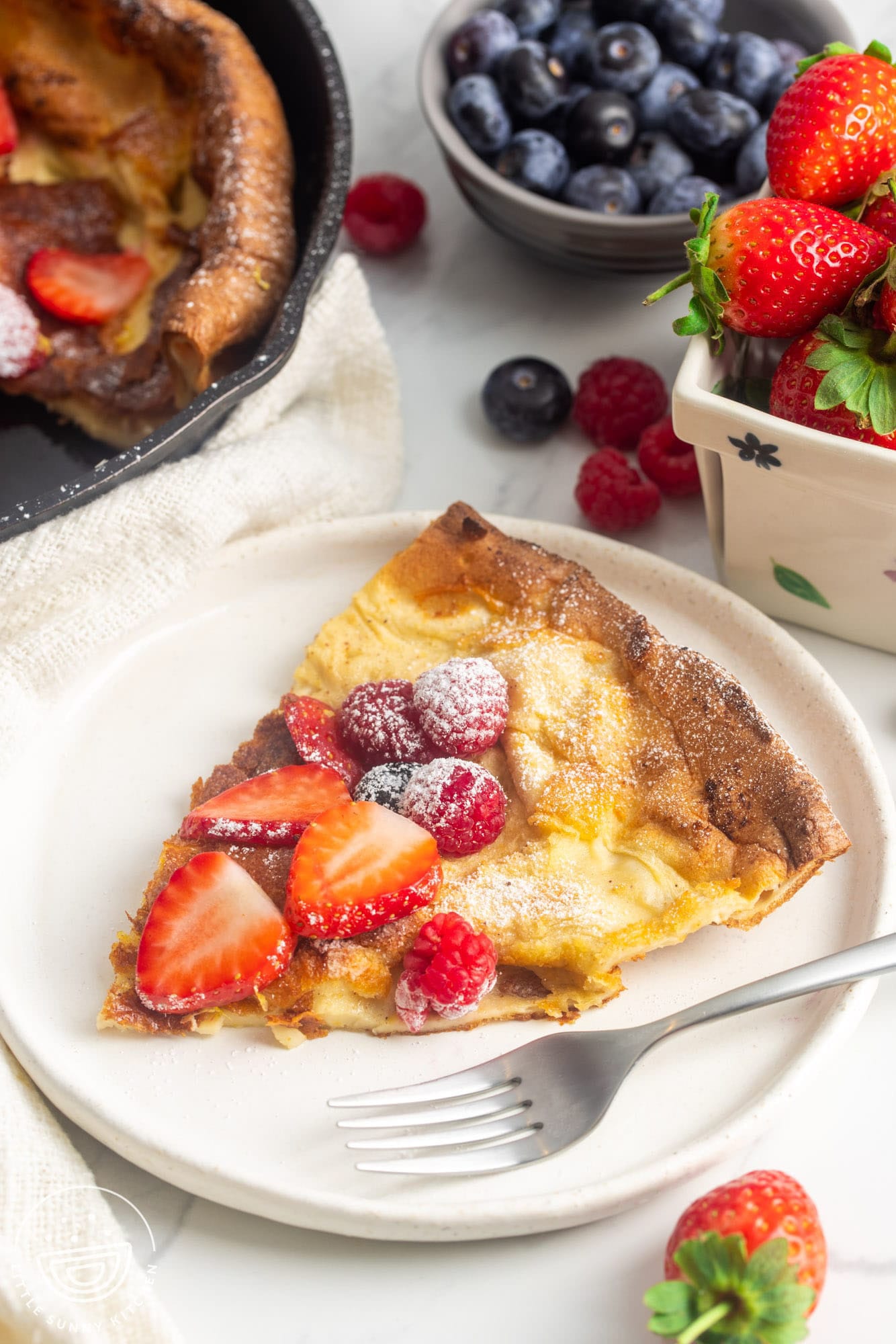 a wedge shaped slice of a dutch baby pancake on a plate with a fork.